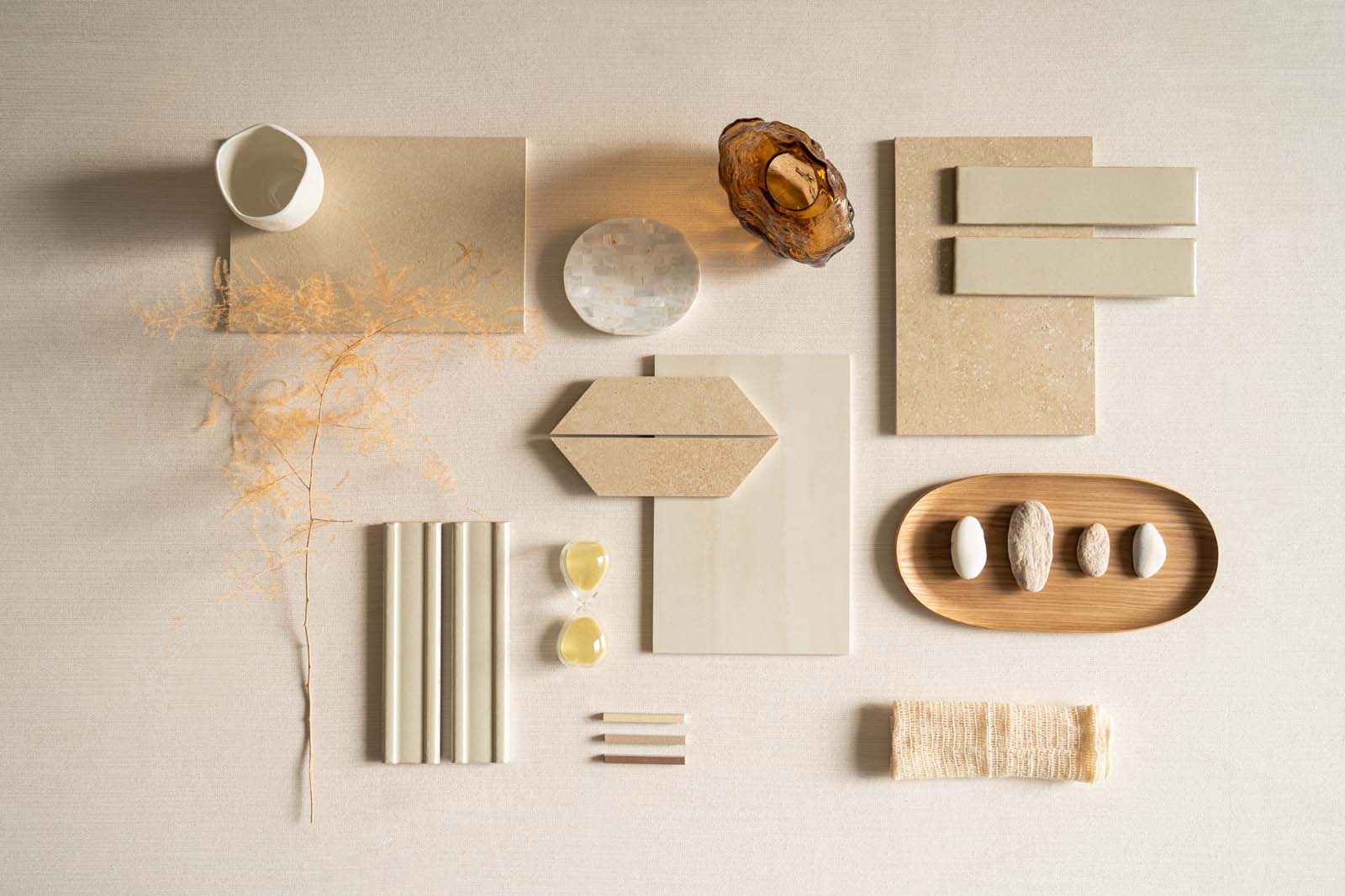 Composizione di materiali neutri: piastrelle, vasi, conchiglie, e decorazioni botaniche su un sfondo chiaro.